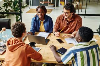 Two coworkers sitting in front of laptop and looking at colleague